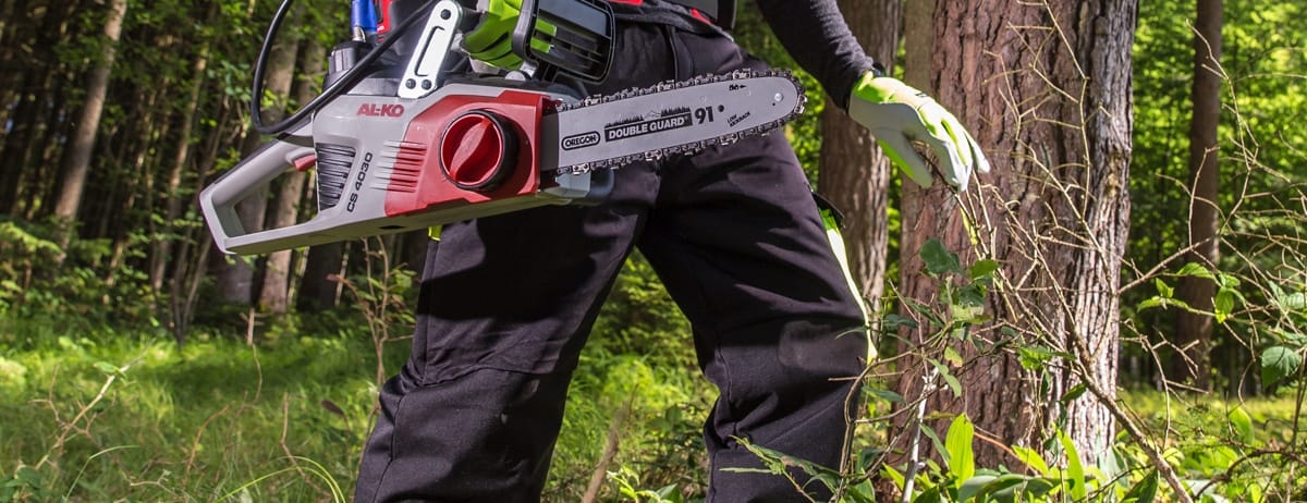 An AL-KO battery chainsaw in use in woodland